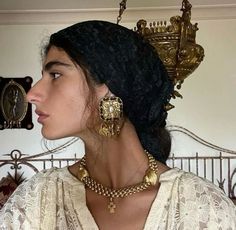 a woman wearing gold jewelry in front of a wall with ornate ornaments on it's head