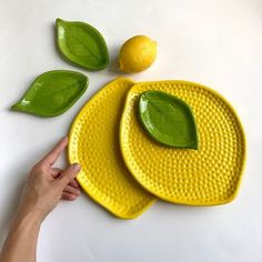 two yellow plates with green leaves and a lemon on the top one is pointing at it