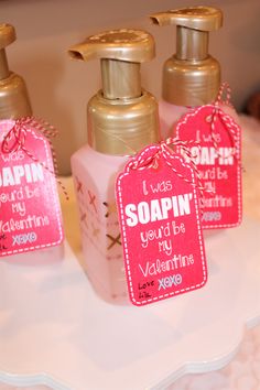 three pink soap bottles with tags on them sitting on a white tablecloth covered table