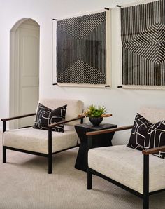 two white chairs sitting next to each other in front of paintings on the wall above them