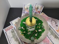 a green candle sitting on top of a metal plate filled with money next to a stack of twenty dollar bills