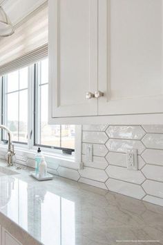 a kitchen with white cabinets and marble counter tops in front of a large open window