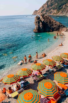 many people are on the beach with orange and blue umbrellas