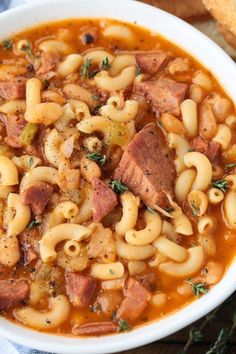 a white bowl filled with pasta and meat soup on top of a blue towel next to bread