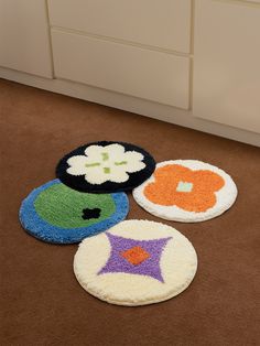 four round rugs on the floor with flowers and stars in them, all made out of yarn