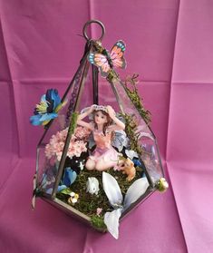 a glass terrarium filled with lots of flowers and fairy figurines sitting on top of it