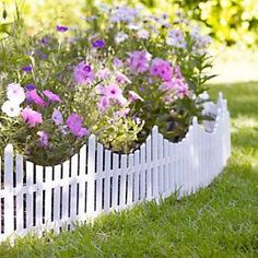 a white picket fence with purple flowers in the center and green grass on the other side