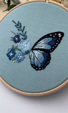 a blue and black butterfly with flowers on it's back is sitting in front of an embroidery hoop