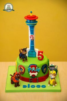 a birthday cake for a five year old boy with paw patrol characters on it and a dog tower in the background