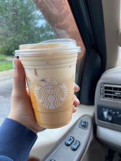 a woman holding up a cup of coffee in her hand while sitting in the backseat of a car