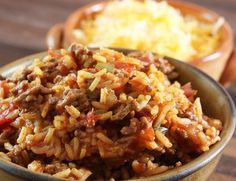 a bowl filled with rice and meat on top of a wooden table next to bread