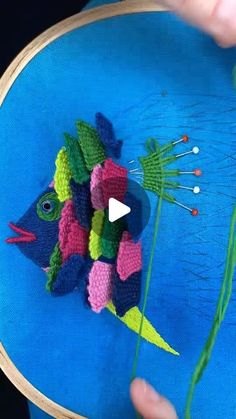 someone is stitching a fish on a piece of fabric with needles and thread in front of a blue background