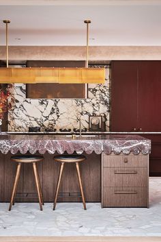 a kitchen with marble counter tops and stools in front of an island that has two wooden barstools on it