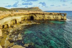 people are standing on the edge of an ocean cliff with clear blue water and cliffs in the background