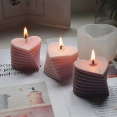 three pink candles sitting on top of a table next to an open book and magazine