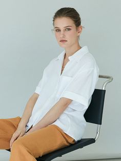 a woman sitting in a chair with her legs crossed and wearing brown pants, white shirt and black shoes