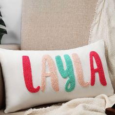 a white pillow with the word laya on it sitting next to a beige chair