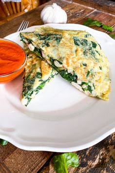 two pieces of omelet on a white plate next to a bowl of tomato sauce