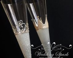 two champagne flutes with white and silver decorations on them are sitting side by side in front of a black background