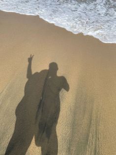 a shadow of a person standing on the beach with his arms in the air,