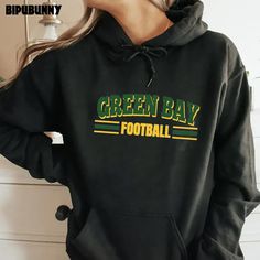 a woman wearing a black hoodie with green bay football written on the front and bottom