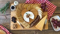 a heart shaped cheese board with crackers, grapes and nuts on it next to other snacks