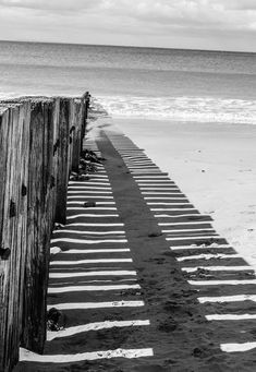 a black and white photo of a wooden fence on the beach