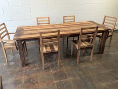 a wooden table with chairs around it on the floor in front of a brick wall