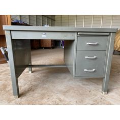 a gray desk with three drawers on the top and bottom, sitting in a garage