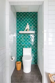 a white toilet sitting in a bathroom next to a wooden trash can and tiled walls