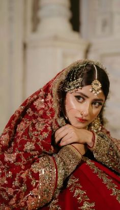 a woman in a red and gold bridal outfit with her hands on her chest