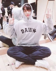 a young man sitting on the floor with his hands in the air and wearing a hoodie