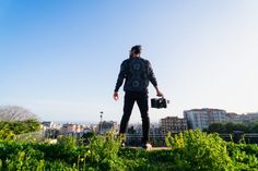 a man standing on top of a lush green field next to tall buildings and trees