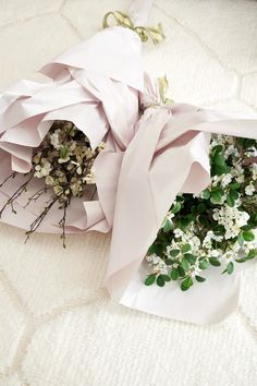 a bouquet of white flowers wrapped in pink paper on a bed sheet covered with fabric