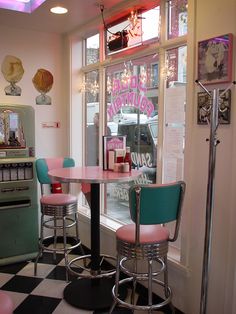 an old fashioned diner with pink and blue chairs, checkered flooring and neon lights