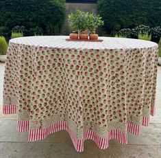 a round table with red and white flowers on it in the middle of a garden