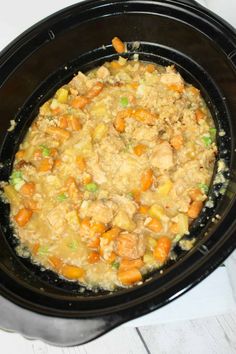 a crock pot filled with chicken and carrots on top of a white table