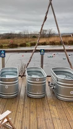 three metal buckets sitting on top of a wooden deck next to a body of water