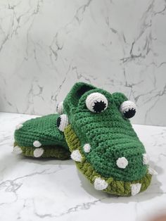 two crocheted alligator slippers with eyes and nose are sitting on a marble surface