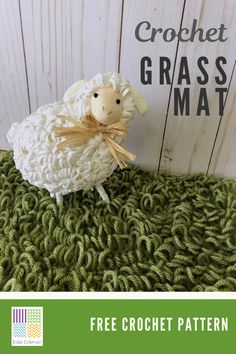 a crocheted sheep sitting on top of a green blanket next to a wooden sign