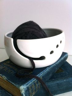 a white bowl sitting on top of a book next to a ball of black yarn