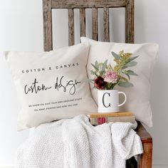 two pillows on a chair with flowers in a mug and a book next to them