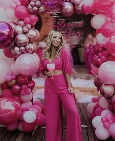 a woman standing in front of a pink backdrop with balloons and coffee cups on it