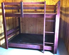 a wooden bunk bed in a room with wood paneling on the walls and floor