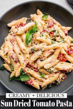 creamy and delicious sun dried tomato pasta with spinach leaves in a black bowl on a gray surface