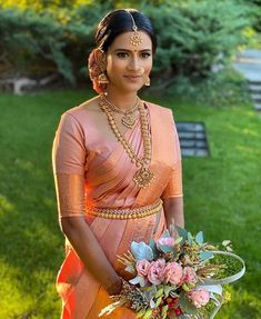 a woman in an orange sari holding a bouquet of flowers on her wedding day