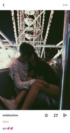 a man and woman sitting on a bench in front of a ferris wheel at night