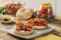 two small sandwiches with tomatoes on them sit on a plate next to some bread and olives