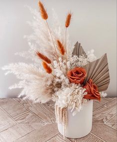 an arrangement of dried flowers in a white vase on a wooden table with a fan