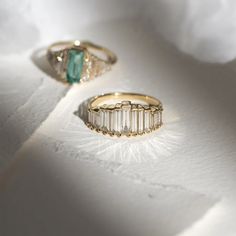 two gold rings with emeralds and diamonds on white fabric, close up view from above